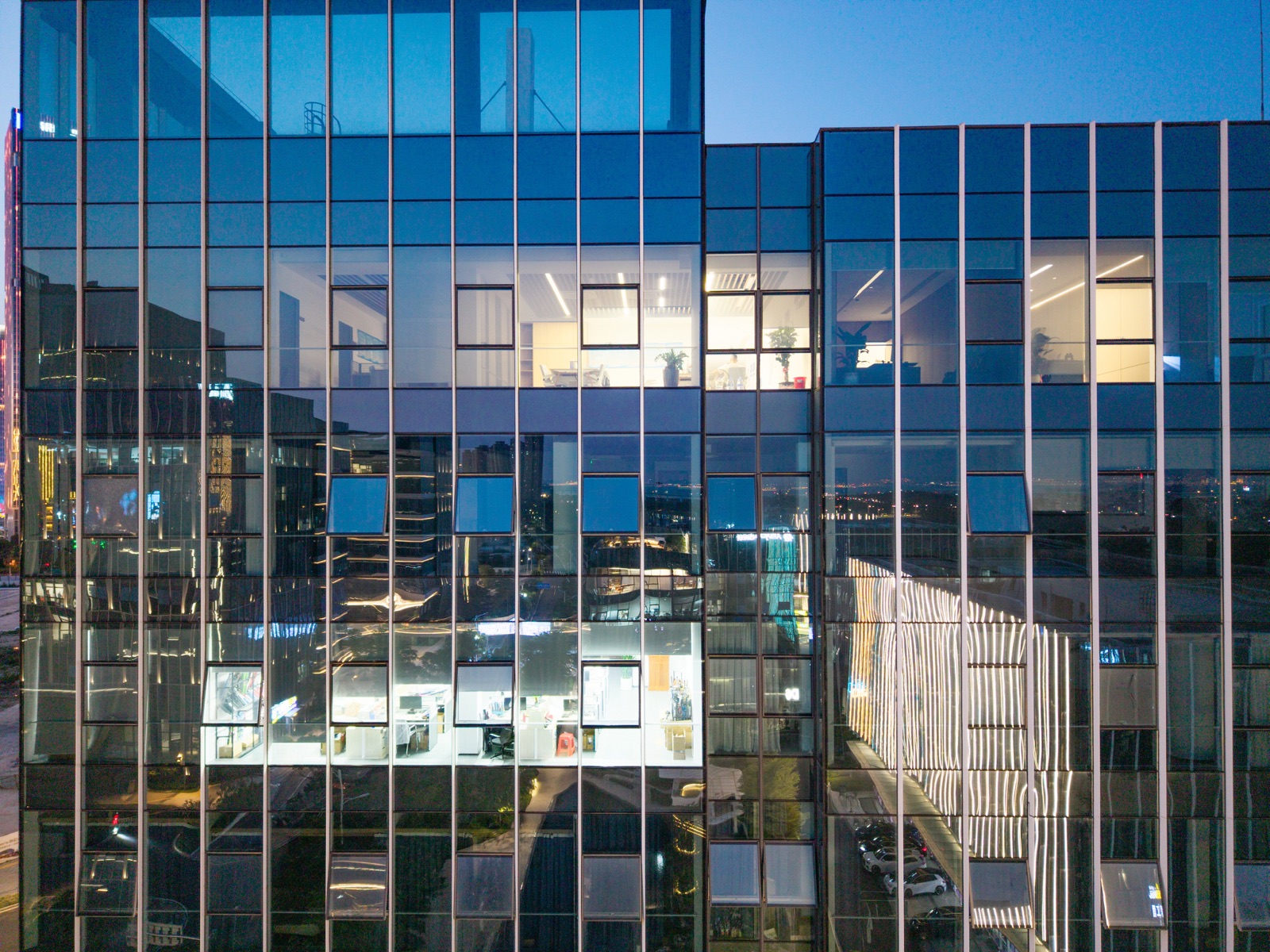 A glass office building at dusk with a few floors lit and the rest dark