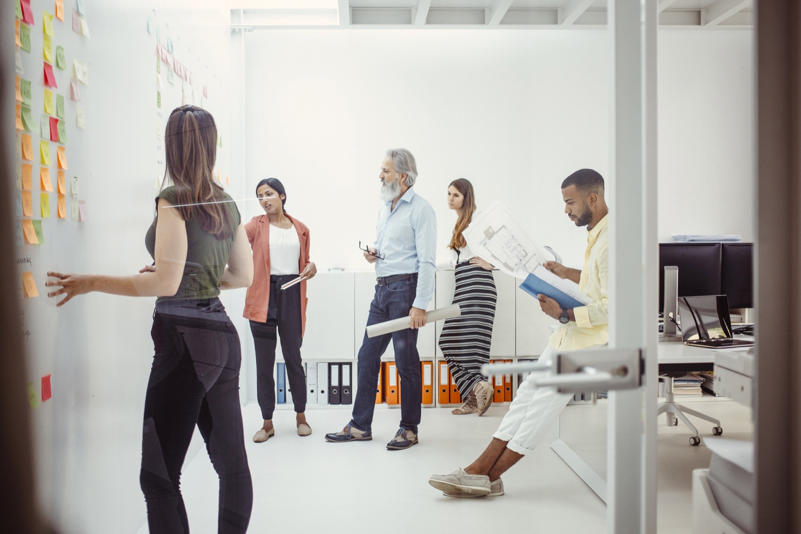 A team of five planning together around a wall of sticky notes in a bright office